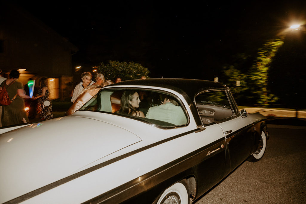 bride and groom driving off in vintage car